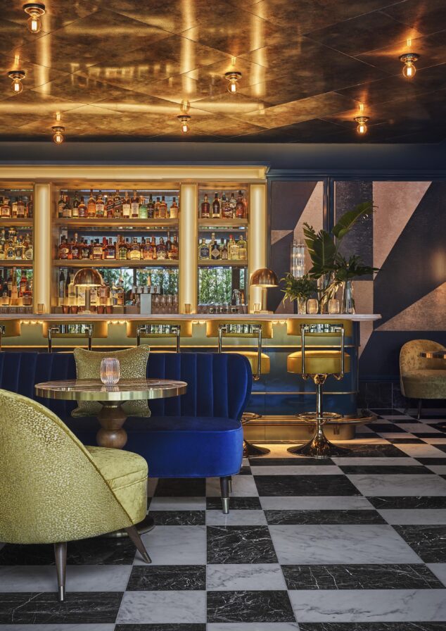 Stylish Bar Pendry interior with checkered floor, blue and green seating, a well-stocked backlit bar, and warm lighting.