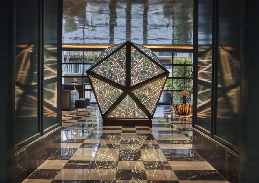 Geometric sculpture created by Cao and Perrot, titled the "Sunset Jewel" with intricate patterns in the Pendry West Hollywood lobby entry way. Reflective marble floor and large windows in the background.