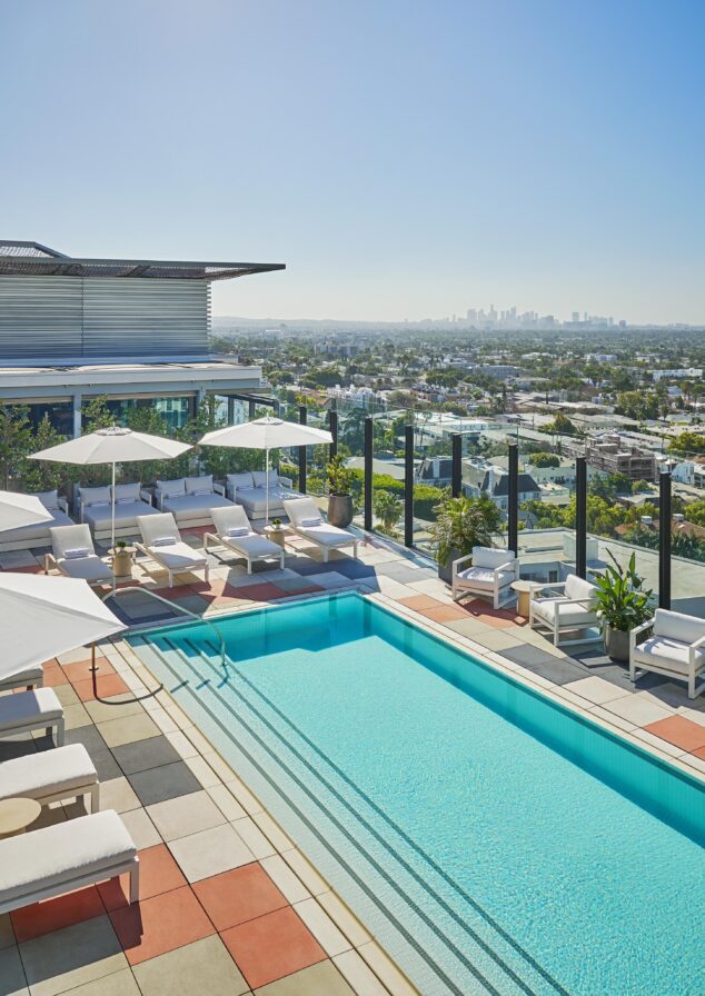 West Hollywood rooftop Pendry hotels resort pool with lounge chairs and umbrellas, overlooking a cityscape under a clear blue sky.