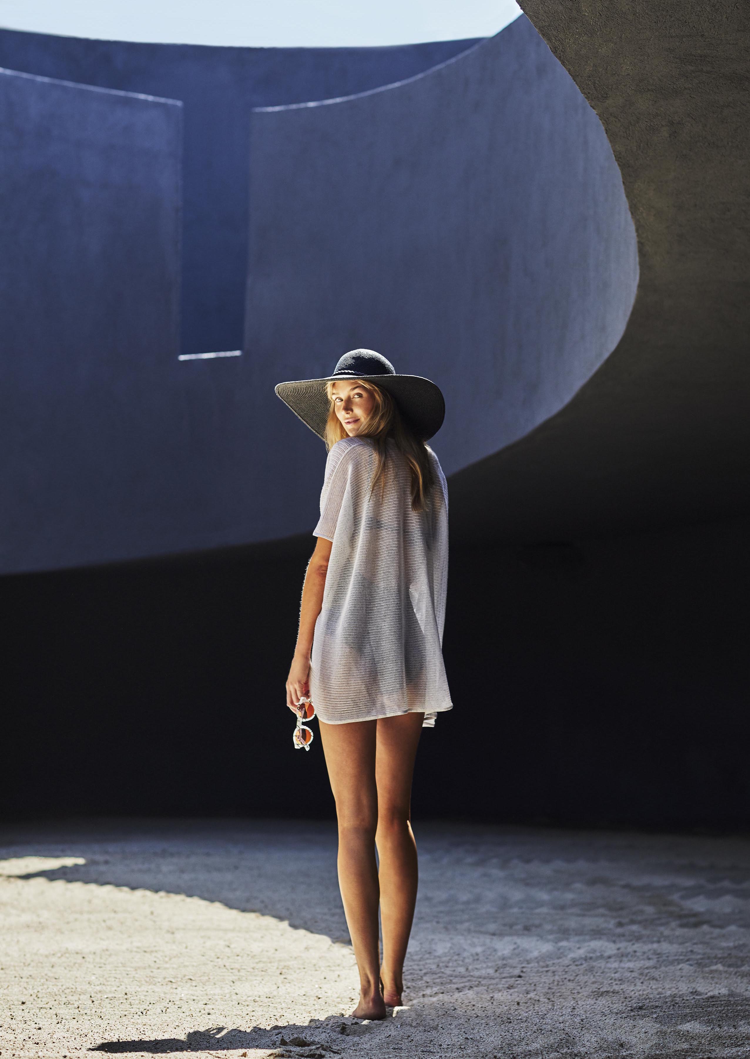 Woman wearing beach coverup looks over shoulder and standing beneath rounded architectural structure at Viceroy Los Cabos courtyard.