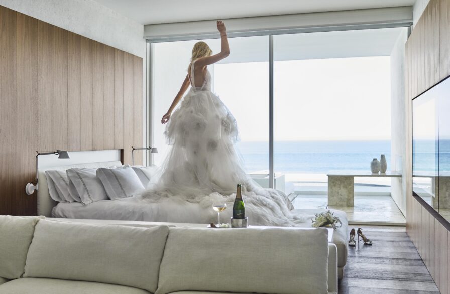 woman jumping on hotel suite bed wearing wedding dress.