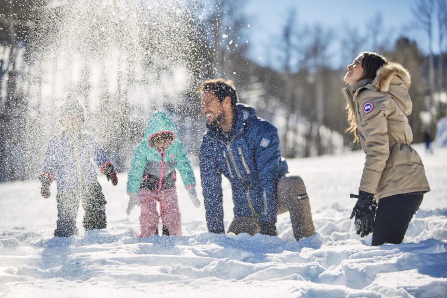 Family playing in snow, trees surrounding Montana mountains