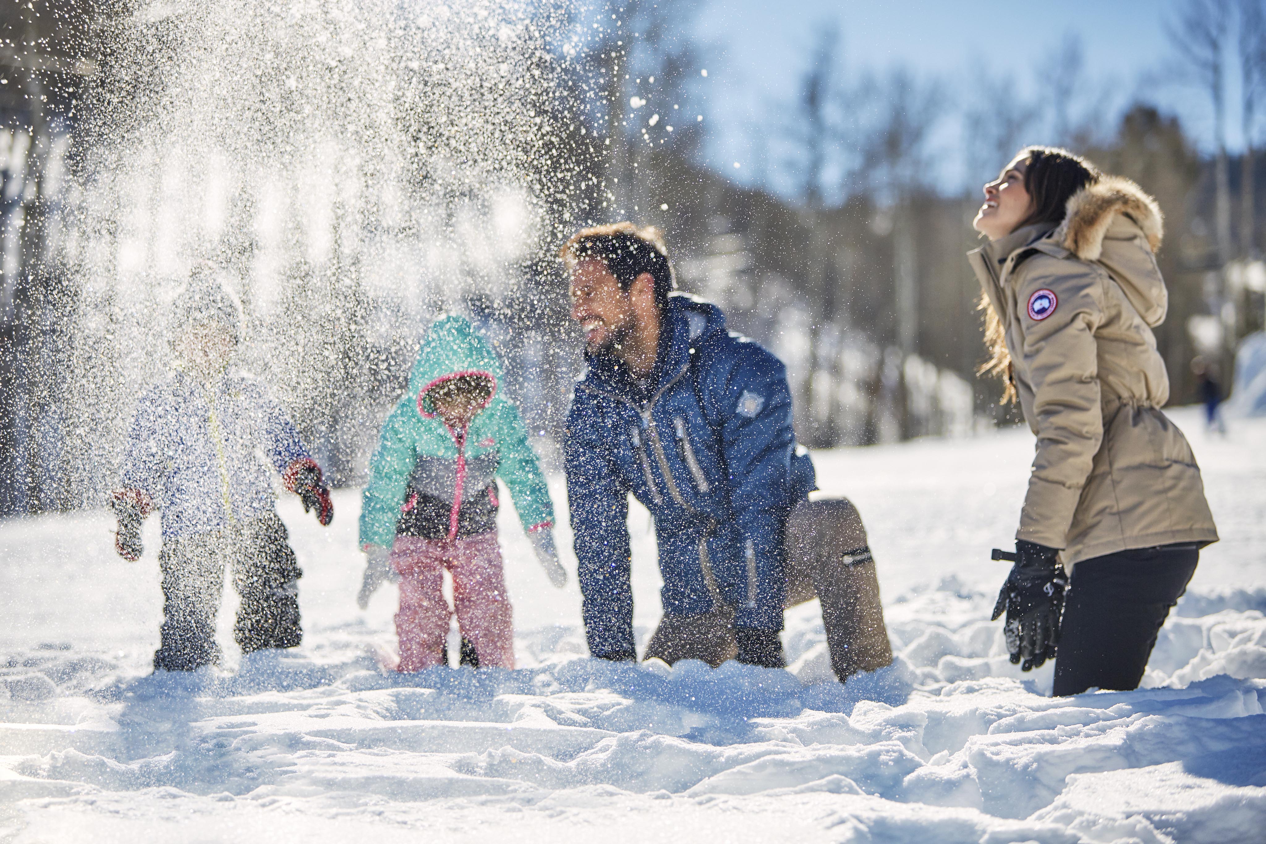 Family playing in snow, trees surrounding Montana mountains