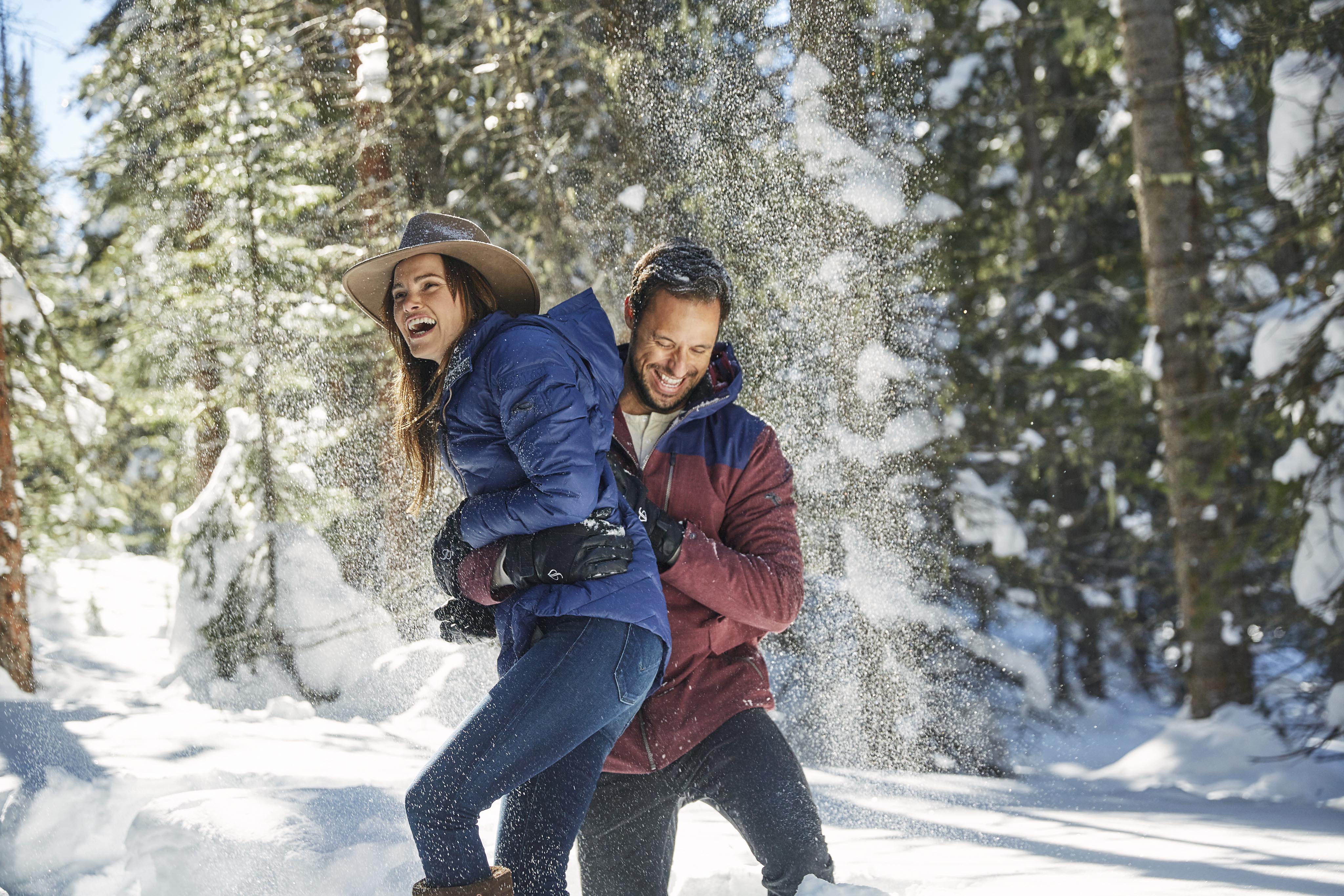 couple playing in snow, pine trees behind