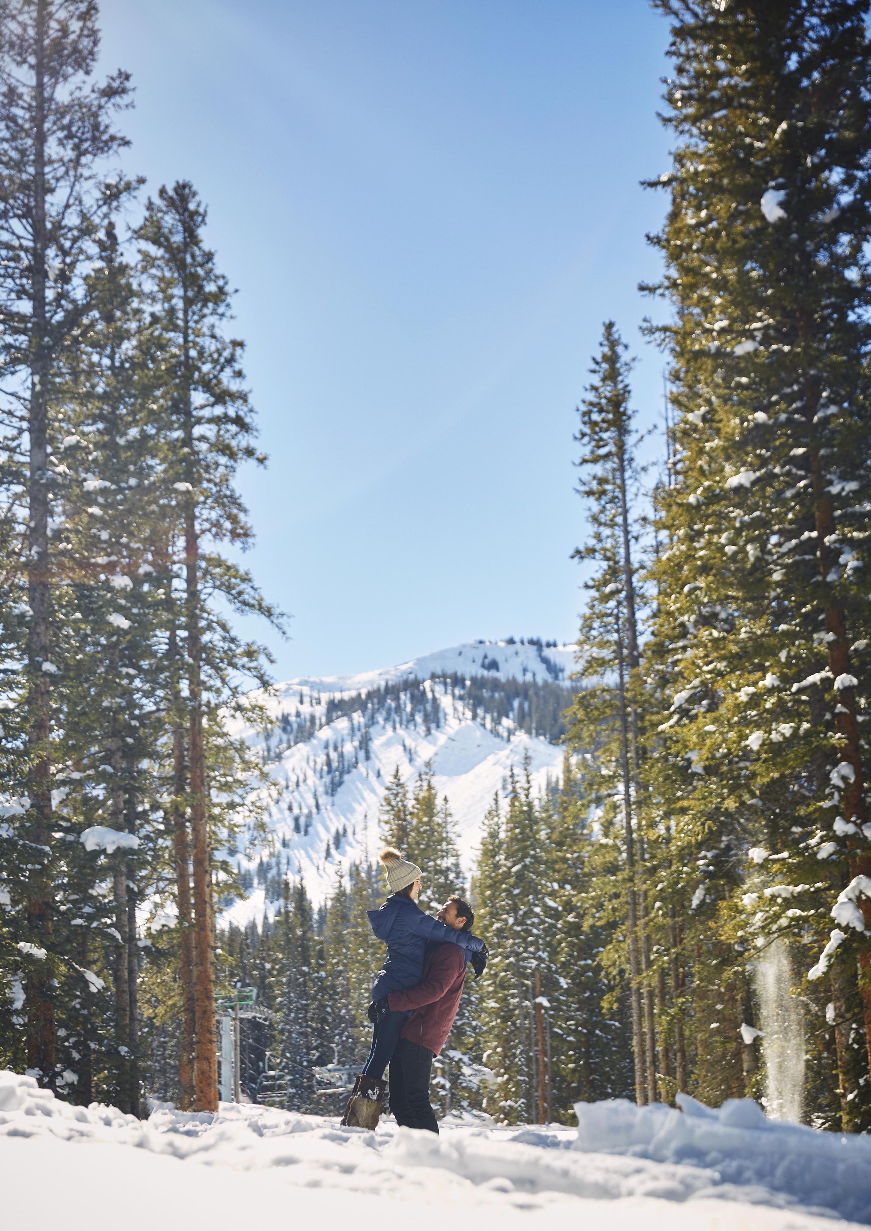 A joyful couple embraced between snowy mountain pine trees with Aspen mountain backdrop.