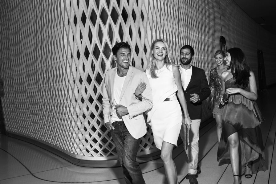 A group of five well-dressed people walk together indoors, smiling and laughing in front of a patterned wall, capturing the vibrant atmosphere of luxury hotel and resort photography in the Middle East.